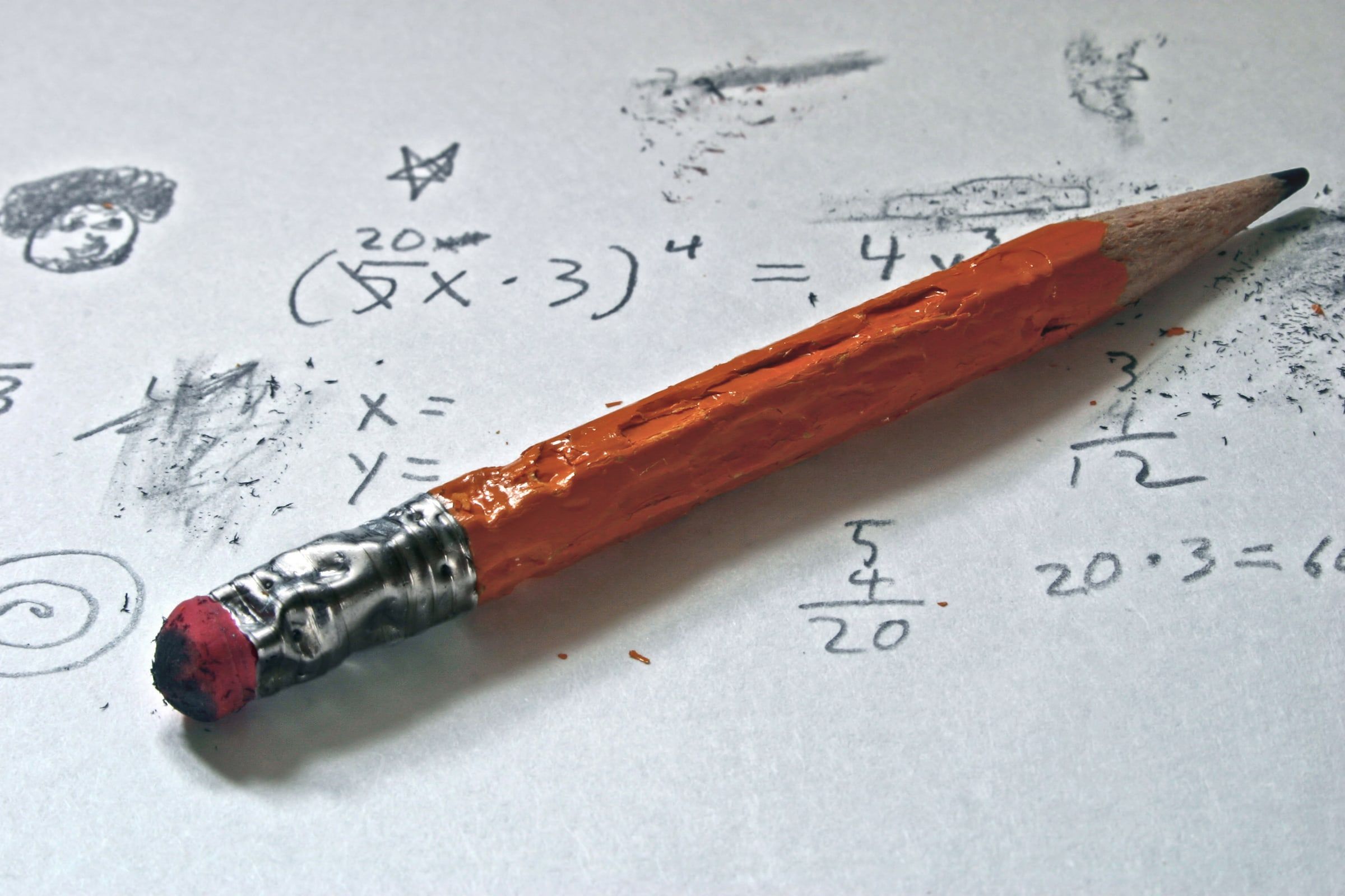 A worn orange pencil lying on paper covered in math problems and doodles