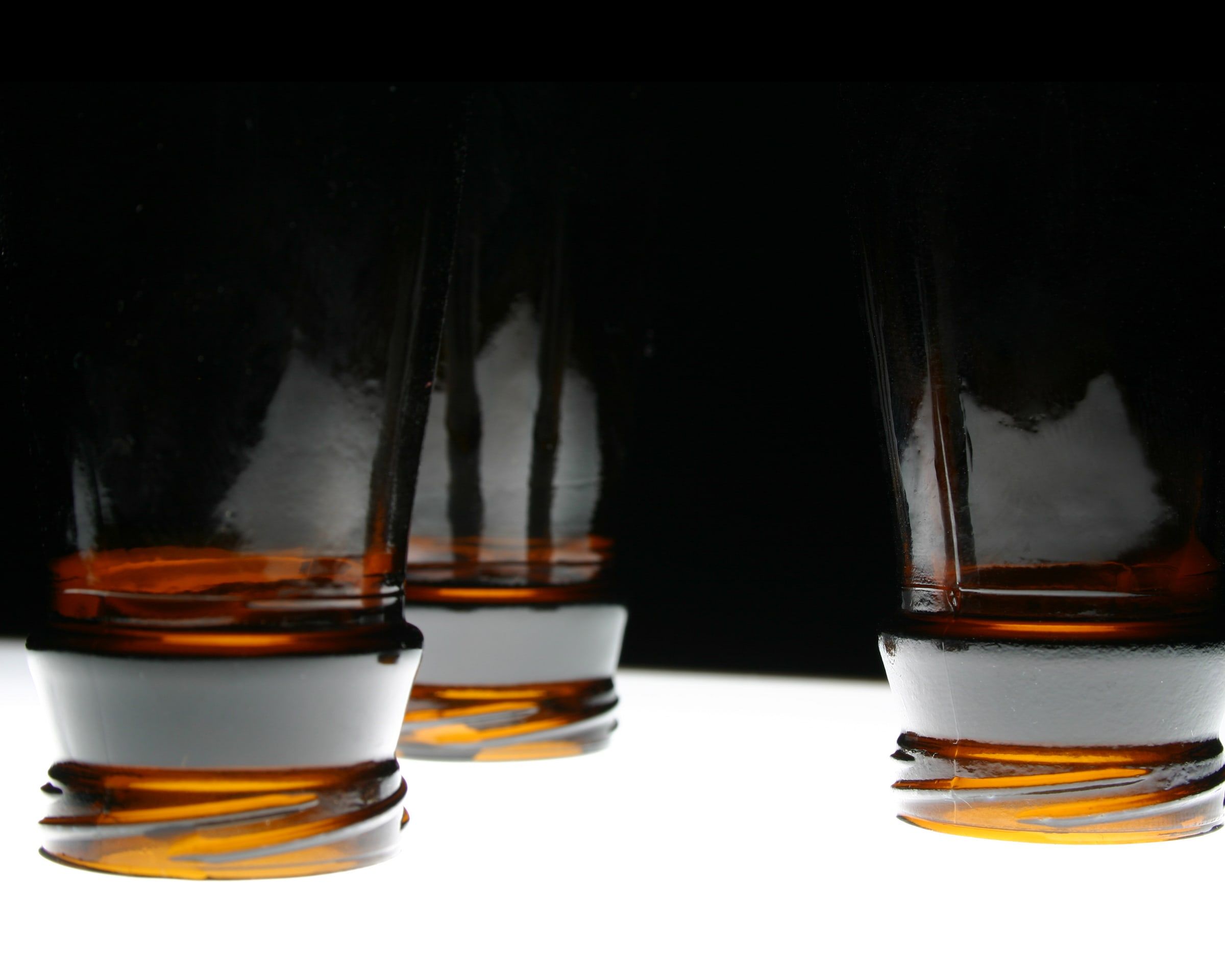 Three backlit amber glass bottles on a white surface against black
